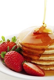 pancakes and strawberries with maple syrup pouring over them