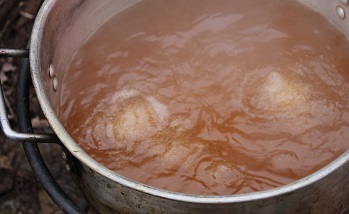 dark brown boiling maple syrup in large kettle.
