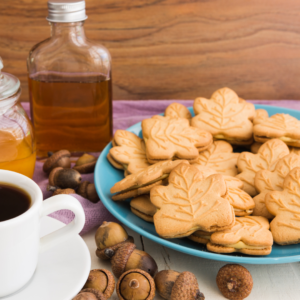 blue plate with maple leaf shaped cookies with maple cream filling and a half-filled bottle of maple syrup sitting beside it.
